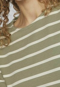 Oliwkowy t-shirt w białe poziome paski, z klasycznym okrągłym dekoltem i miękkim, lekkim materiałem.