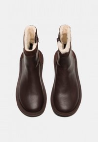 Botas de tobillo de cuero marrón con forro de piel de oveja, cierre de cremallera, punta redonda y suela plana de goma. Textura suave y diseño minimalista.