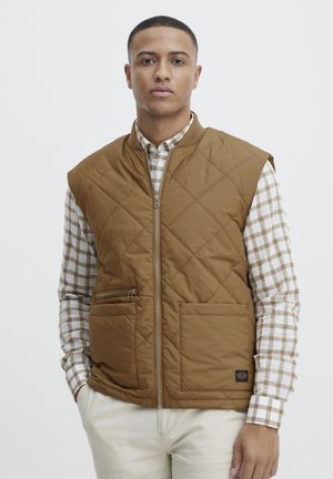 Quilted brown puffer vest with a zippered front, side pockets, and a standing collar, layered over a checkered shirt with long sleeves.
