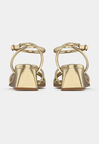 Sandale metalice aurii cu toc înalt și pătrat, curea la gleznă și curele încrucișate. Textură netedă cu finisaj lucios.