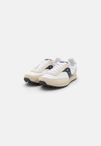 Beige og hvide atletiske sko med en overdel i ruskind og mesh, sorte detaljer, hvide snørebånd og en tekstureret gummisål.