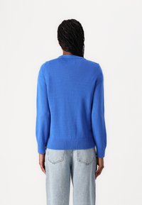 Blue knitted sweater with long sleeves, ribbed cuffs and hem, round neckline, smooth texture, and fitted silhouette, paired with light jeans.