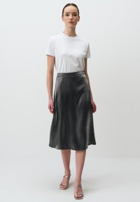 Gonna in satin argentato con una silhouette fluida, abbinata a una maglietta bianca semplice. L'outfit presenta una leggera lucentezza e un design minimalista.