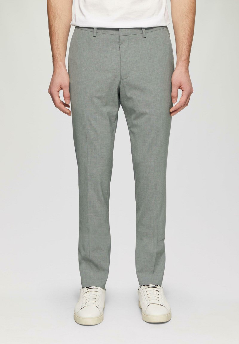 Helles graue, maßgeschneiderte Hose, schlanke Passform, strukturierter Stoff, flacher Vorderteil, Gürtelschlaufen, getragen mit weißen Sneakers.