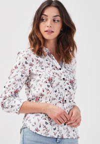 Chemise blanche à boutons avec un motif floral et de papillons en rouge et gris. Dotée d'un col pointu et de manches trois-quarts.
