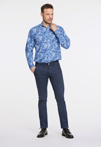 Blaues, blumiges Musterhemd mit langen Ärmeln, kombiniert mit marineblauen Chinos und schwarzen Schuhen; glattes Material und taillierter Schnitt.