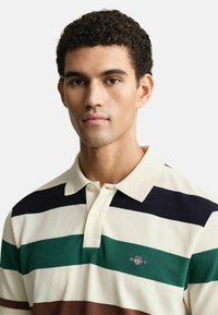 Gestreepte polo shirt met brede horizontale strepen in crème, donkerblauw, groen en bruin. Inclusief een kraag en een knoopsluiting met twee knopen.