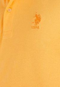 Rumena polo majica iz teksturirane tkanine z izvezenim logotipom USPA. Dva gumba spredaj, klasična oblika ovratnika.