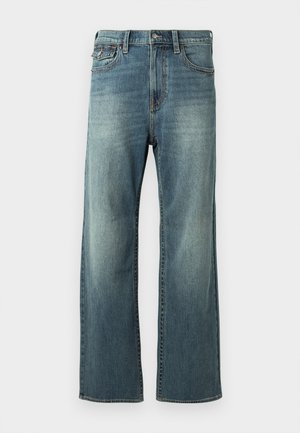 Világoskék farmernadrág, egyenes lábakkal, enyhe kopással, öt zsebbel és övhurkokkal. Varsóvarrásos részletekkel és gombos zárszerkezettel rendelkezik.