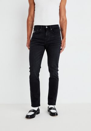 Zwarte denim jeans met een slim fit, voorzien van vijf zakken, stiksels en een medium taille, gecombineerd met zwarte instappers en witte sokken.