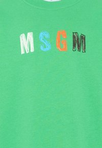 Tela verde con las letras "MSGM" en blanco, azul, naranja y negro, dispuestas en fila con una fuente de estilo boceto.