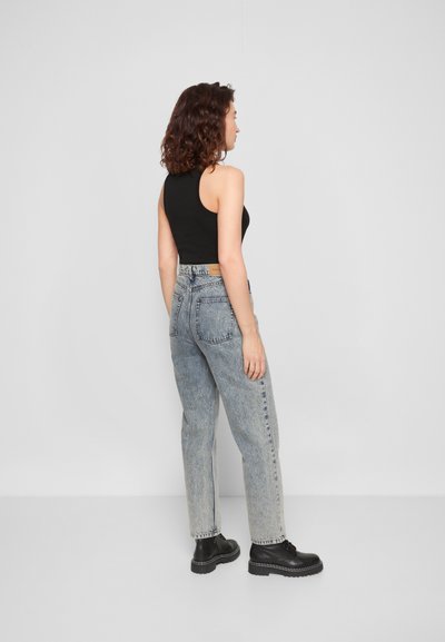 Top preto sem mangas combinado com jeans azuis desbotados de cintura alta e botas pretas de atacadores, exibindo um ajustamento relaxado e um design de perna reta.