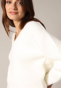 Witte, fluffy trui met een V-hals en oversized mouwen, met een zachte textuur en een relaxte fit.