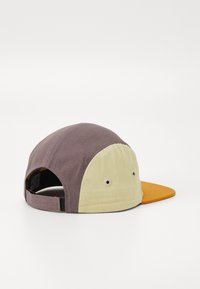 Casquette multicolore avec une couronne arrondie en marron et jaune clair, dotée d'un pic orange et de perforations de ventilation sur les côtés.