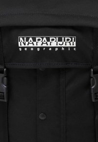 Mochila de tela negra con el logo en blanco de "Napapijri Geographic", con correas ajustables y una superficie texturizada.
