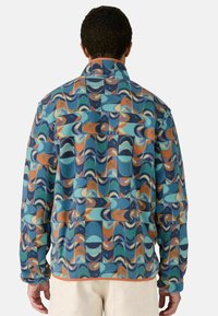 Chaqueta de forro polar con un patrón geométrico multicolor, que incluye tonos de azul, naranja y púrpura. Cuenta con un cuello tipo solapa y puños elásticos.