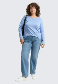 Lichtblauw langemouwshirt gecombineerd met lichtblauwe rechte jeans. Het model draagt witte sneakers en heeft een zwarte schoudertas.