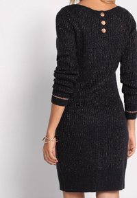 Robe en tricot côtelé navy avec trois boutons métalliques au dos, présentant des manches longues et une silhouette ajustée, accentuée d'un subtil éclat.