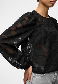 Juoda permatoma palaidinė su gėlių siuvinėjimu, ilgomis pūstomis rankovėmis ir apvaliu iškirpimu. Audinys turi tekstūruotą, sluoksniuotą dizainą.