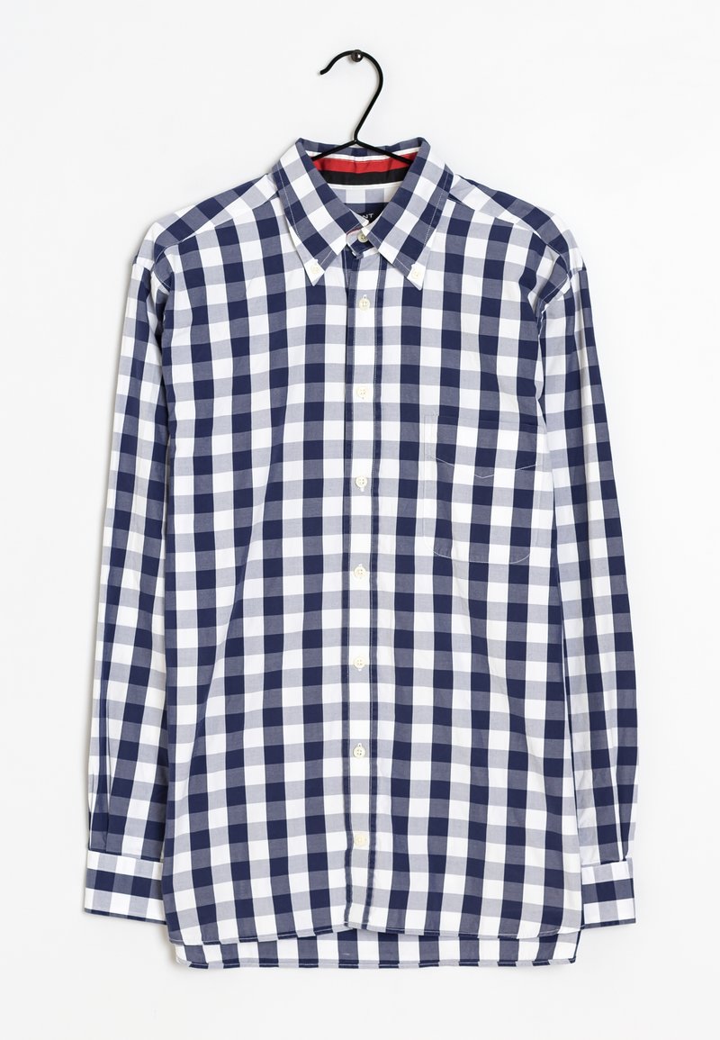 Chemise à manches longues boutonnée avec un motif à carreaux bleu marine et blanc accrochée à un cintre noir.
