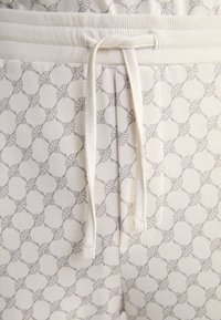 Jogging léger beige avec un motif géométrique texturé en gris. Il comporte une taille côtelée et un cordon de serrage pour un ajustement réglable.