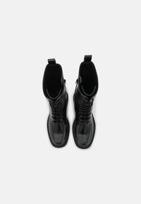 Bottes en cuir noir à lacets avec une tige haute, une texture lisse, un bout arrondi et des fermetures éclair doubles sur les côtés. Équipées de deux languettes pour faciliter l'enfilage.