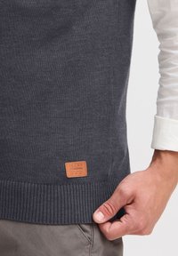 Dunkelgrauer Strickpullover mit geripptem Saum und einer Lederpatch mit der Aufschrift "BLEND". Hat eine glatte Textur und ein figurnahes Design.