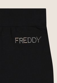 Leggings noirs avec une texture lisse et une large ceinture. Le mot "FREDDY" est orné d'accents semblables à des cristaux.
