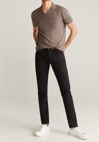 Hnědá texturovaná polo tričko s krátkým rukávem a výstřihem do V, doplněné úzkými černými kalhotami a bílými teniskami, obsahující pásek se stříbrnou sponou.