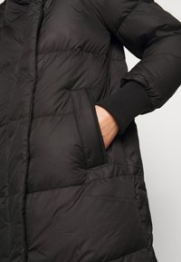 Svart pufferjacka med quiltat mönster, försedd med sidofickor och ribbade ärmslut. Snygg design med hög krage för extra värme.