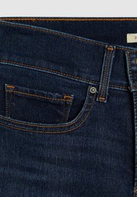 Tmavě modré džíny s oranžovým šitím, přední kapsou s zakřivenými okraji a kovovým knoflíkem na pase.