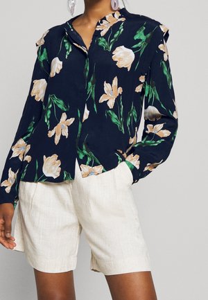Person wearing a navy floral long-sleeve blouse with beige flowers and light beige knee-length shorts.