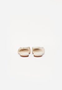 Sandales tressées beiges avec des semelles plates, des talons ouverts et une surface texturée. Des semelles en cuir souple et une semelle extérieure lisse couleur tan complètent le design.
