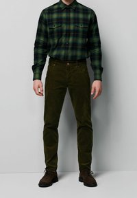 Zielono-czarna flanelowa koszula w kratę z dwoma kieszeniami na piersi, zestawiona z oliwkowozielonymi sztruksowymi spodniami i brązowymi zamszowymi butami.