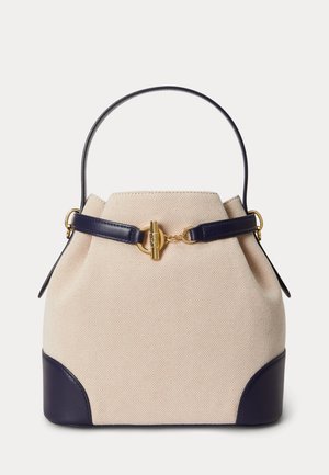 Geantă tip sac din material bej cu accente din piele albastru închis, mâner simplu și închizătoare cu tăgliță aurie pe un fundal simplu.