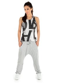 Mouwloos shirt in wit en zwart met grafische print; grijze harempants met zijzakken; model draagt witte sneakers.