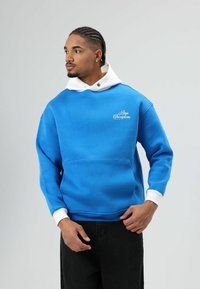 Blauwe hoodie met een witte trekkoord en kraag, voorzien van een voorzak en de tekst "Boys Champions" in het wit op de linkerborst.