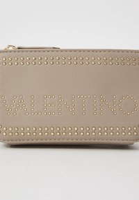 Bēšs ādas maks ar zelta kniedēm un izspiestu "VALENTINO" logo priekšpusē. Augšpusē ir rāvējslēdzēja aizdare, gluda tekstūra.