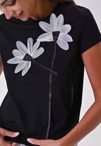 Zwarte t-shirt met twee grote witte bloemapplicaties met zwarte centra,accentueert met een zwart lintdetail langs de zijnaad.