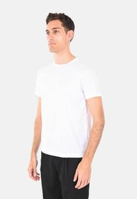 T-shirt bianca a maniche corte in cotone, con colletto rotondo classico e design semplice, indossata con pantaloni neri.