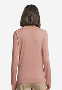 Ljusrosa långärmad tröja med slät textur, rundad hals och ribbat nederkant, med en enkel design och inga synliga mönster.