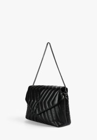 Bolso de mano de cuero acolchado negro con solapa plegable y cadena. Presenta una textura en zigzag, forma compacta y estructurada, y un branding sutil.