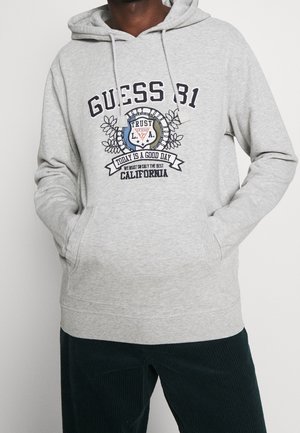 Grauer Hoodie mit einem grafischen Design, das "GUESS 81" und florale Akzente zeigt. Enthält eine Fronttasche und eine Kapuze mit Kordelzug. Aus Baumwollmischung.