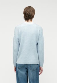 Svijetloplava rebrasta pletiva s dugim rukavima, opuštenog kroja i okruglim izrezom, u kombinaciji sa svijetloplavim trapericama širokog kroja.