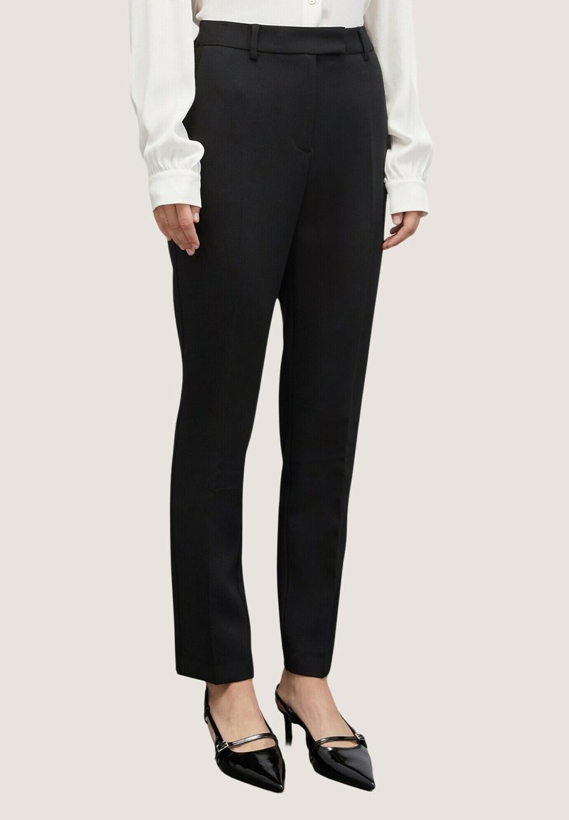 Pantalon noir sur mesure à coupe slim, avec une texture lisse et un motif à fines rayures discrètes. Associé à des talons noirs pointus.