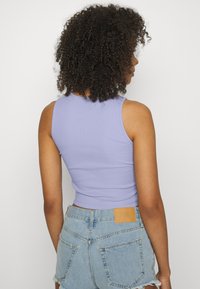 Top cropped lilás claro com textura canelada, combinado com calções de ganga de cintura alta com uma etiqueta de marca em pele e bainha desfiada.