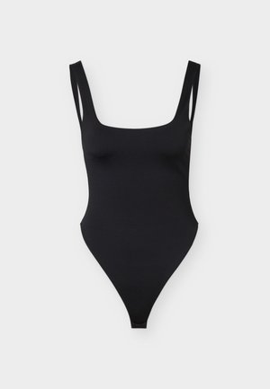 Costum de baie întreg negru, cu decolteu pătrat, bretele duble subțiri și tăieturi înalte la nivelul coapselor, pe un fundal simplu, deschis la culoare.