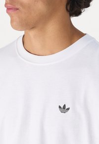 Hvid bomulds T-shirt med et sort Adidas-logo på brystet. Rund halsudskæring med ribbede kanter, glat tekstur og afslappet pasform.