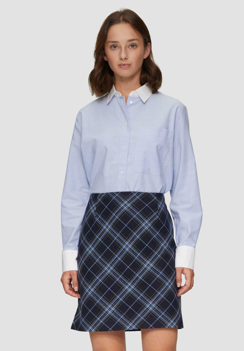 Lichtblauw button-up overhemd met lange mouwen en een zak, gecombineerd met een marineblauwe geruite rok met blauwe en gele accenten.