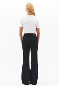 Korkeavyötäröiset mustat leveälahkeiset farkut, joissa on kaksi takataskua ja vyötärölinja. Yhdistettynä lyhythihaisella valkoisella t-paidalla.